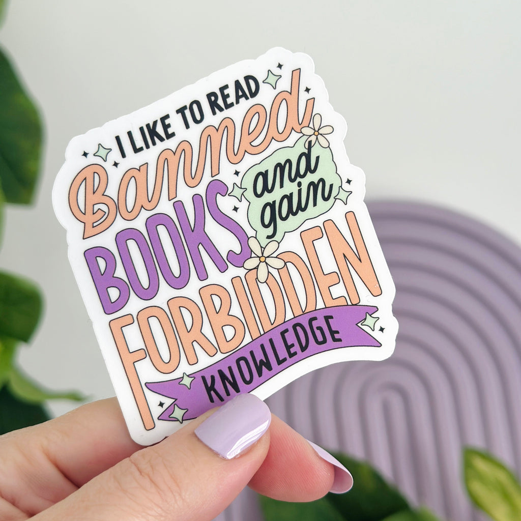 Sticker with text 'I like to read banned books and gain forbidden knowledge' held by a hand.