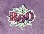 Boo in bright pink and purple written across a black spider web with a white diecut around the sticker